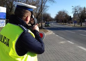 umundurowany policjant dokonuje pomiaru prędkości nadjeżdżających samochodów