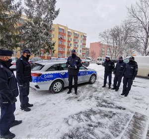 umundurowani policjanci stoją na parkingu, w tle oznakowany radiowóz