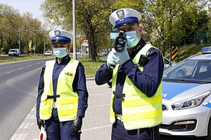 dwoje umundurowanych policjantów stoi przy drodze. jeden z nich dokonuje pomiaru prędkości przy użyciu trzymanego w dłoniach urządzenia