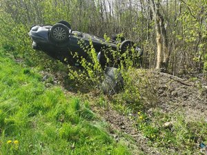 czarny samochód leży na dachu w rowie. Drzwi samochodu są otwarte