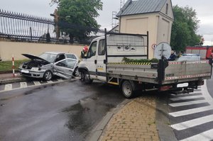 dostawczy samochód iveco z rozbitą białą białą kabiną stoi na wysepce drogowej. Obok niego stoi biały samochód osobowy volkswagen z rozbitym przodem oraz bocznymi drzwiami. w tle oznakowany radiowóz policyjny  _LI