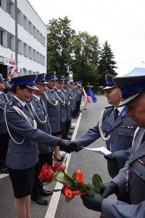 Komendant Powiatowy Policji w Opolu Lubelskim wręcza akty nominacji na wyższe stopnie służbowe awansowanym policjantom. stojący obok pierwszy zastępca komendanta powiatowego policji w Opolu Lubelskim trzyma czerwone róże, które wręcza awansowanym policjantkom.