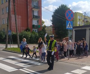 umundurowany policjant przeprowadza przezprzejście dla pieszych gromadę przedszkolaków