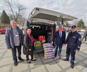 przy samochodzie stoi pierwszy zastępca komendanta powiatowego policji w Opolu lubelskim wraz z delegacją i wójtem gminy Karczmiska Panem Januszem Goliszkiem. w tle widać samochód z artykułami spożywczymi i higienicznymi