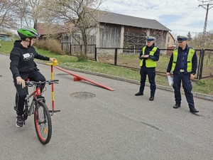 dwaj policjanci patrzą na chłopca, który jadąc na rowerze ustawia element na stoliku