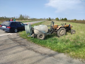 na poboczu drogi stoi ciągnik rolniczy z opryskiwaczem. obok niego stoi granatowy samochód BMW