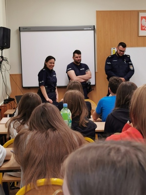 policjanci stoją w sali lekcyjnej przodem do siedzącej w ławkach młodzieży