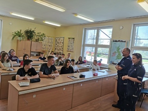 w sali lekcyjnej szkoły dwoje umundurowanych policjantów stoi przodem do słuchającej ich młodzieży.