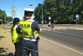 dwoje policjantów patrzy w stronę przechodzących przez jezdnię ludzi
