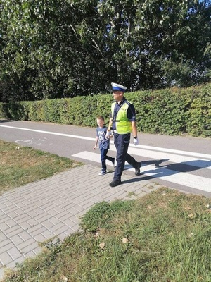 policjant przeprowadza przez pasy chłopca trzymając go za rękę