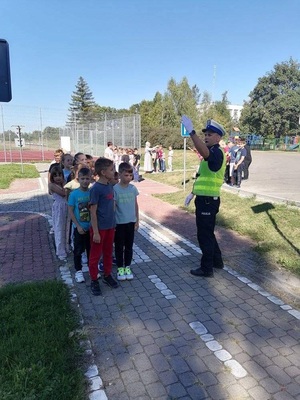 policjant w kamizelce odblaskowej podnosi rękę ucząc dzieci sygnałów, jakie mogą prezentować policjanci