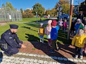 policjant kucając objaśnia dzieciom zasady bezpiecznego przechodzenia przez jezdnię