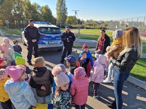 policjanci rozmawiają z dziećmi na dworze. w tle widać policyjny radiowóz