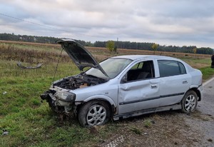 szare auto stoi na poboczu. przód auta jest rozbity, szyba od strony kierowcy jest wybita