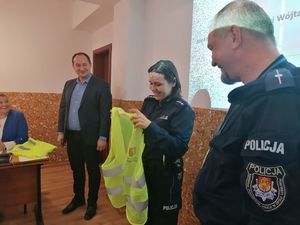 policjantka trzyma w rękach kamizelkę odblaskową. Obok stoi policjant i wójt gminy Wilków