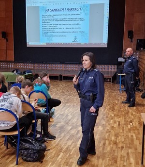 policjantka rozmawia z młodzieżą. w tle widać zasady bezpiecznego zjeżdżania na nartach i sankach