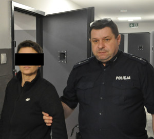 umundurowany policjant prowadzi zatrzymaną kobietę