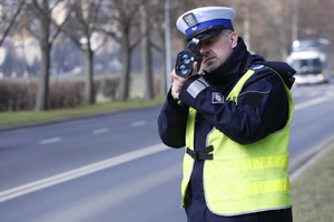 policjant przy drodze dokonuje pomiaru prędkości za pomocą ręcznego miernika prędkości