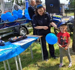 POlicjantaka przymierza dziewczynce czapkę policyjną, dziewczynka trzyma w ręku niebieski balon z napisem policja