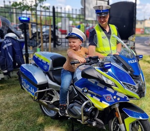 na motocyklu policyjnym siedzi dziecko w czapce policjanta a obok niego stoi policjant ruchu drogowego