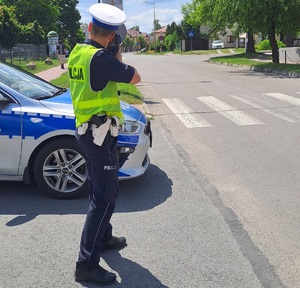 policjant stojący obo radiowozu policyjnego trzymający w ręku radar do pomiaru prędkości