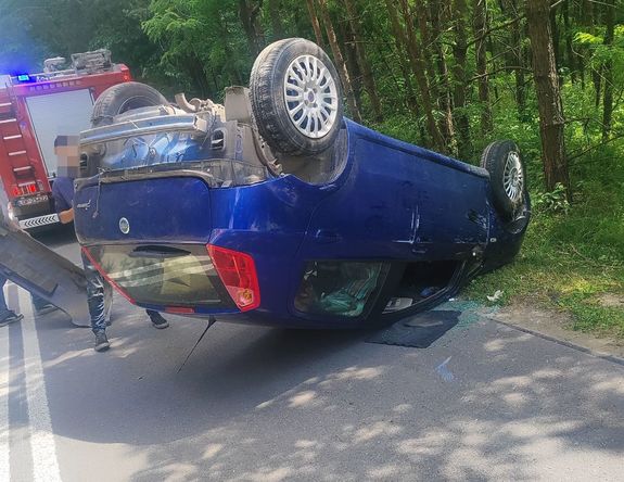 samochód leży na dachu w tle las i samochód straży pożarnej
