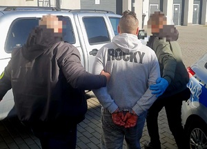 mężczyzna z kajdankami na rękach prowadzony przez policjantów