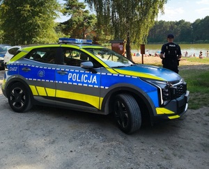 policjant stojący przy radiowozie w tle zbiornik wodny