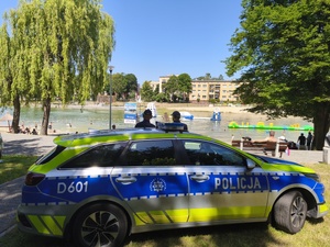 policjanci stoją przy radiowozie w tele widoczne kąpielisko
