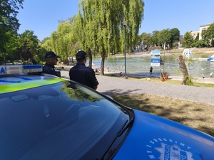 policjanci stoją przy radiowozie w tle widoczne kąpielisko