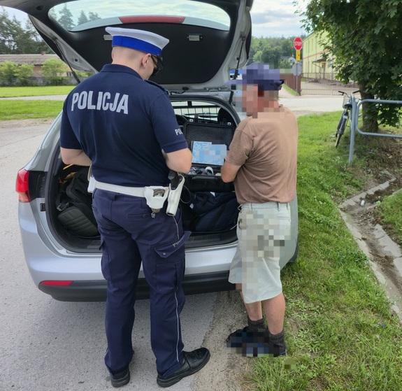 mężczyzna stojący przy radiowozie i policjant