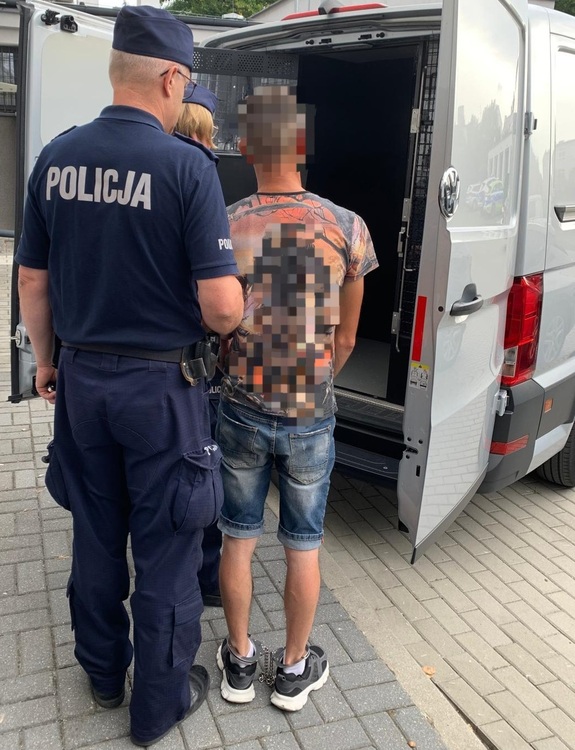 policjanci i mężczyzna z kajdankami na nogach stoją przed radiowozem