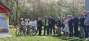 czworo umundurowanych policjantów stoi obok roweru. obok stoją inni zaproszeni goście.