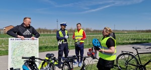 umundurowany policjant stoi obok rowerzystów. jeden z nich trzyma utwardzoną mapę (1)