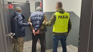 Dwóch policjantów prowadzi zatrzymanego mężczyznę.